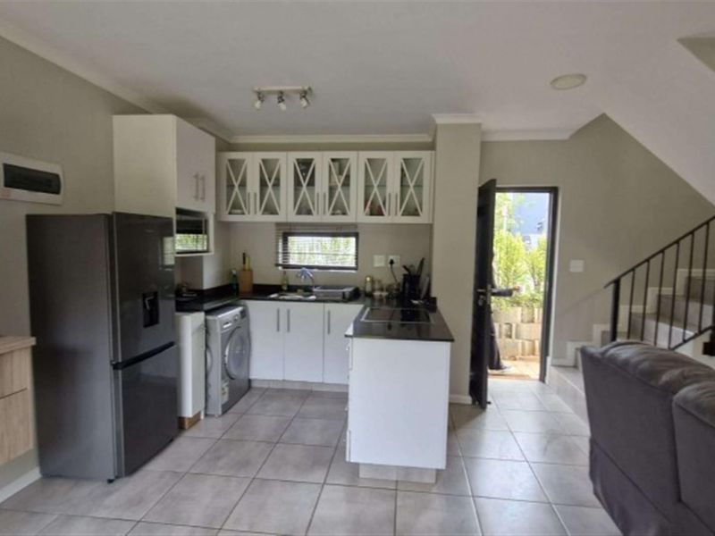 Open-plan kitchen featuring white cabinetry, granite countertops, and tiled flooring, seamlessly connected to the living area and staircase access.