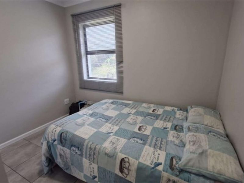 A compact bedroom featuring neutral wall tones, tiled flooring, and a window fitted with a venetian blind.