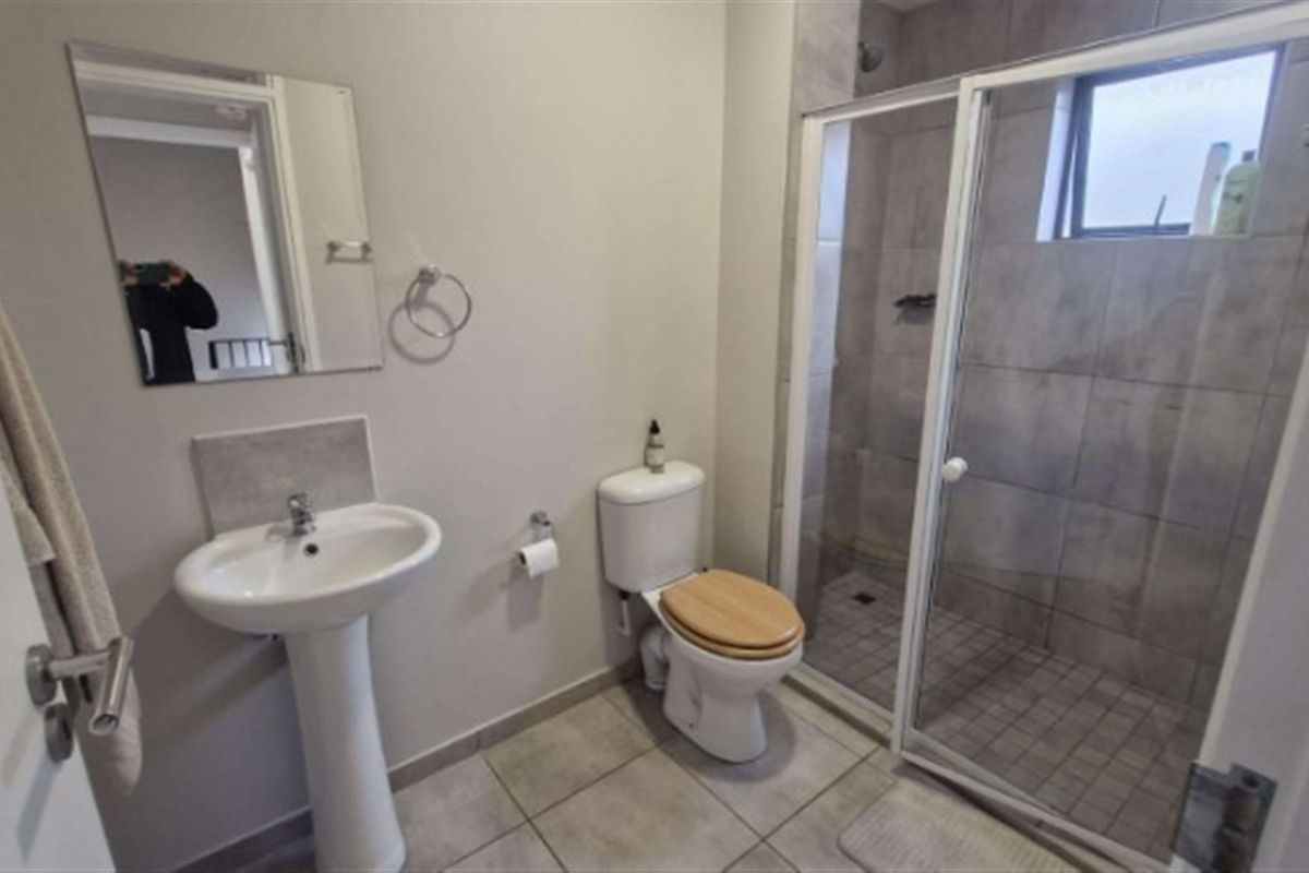 A functional bathroom featuring a pedestal basin, a toilet, and a glass-enclosed shower with neutral wall and floor tiling.