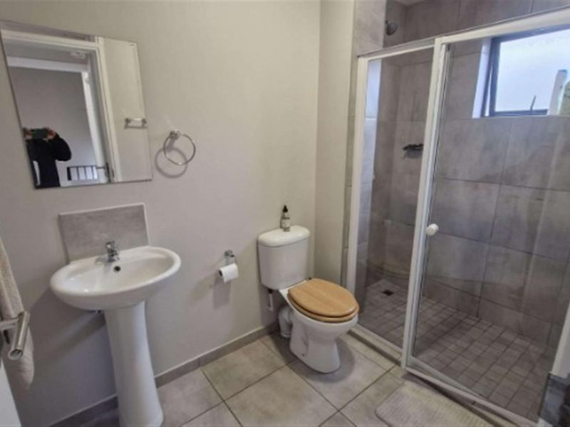 A functional bathroom featuring a pedestal basin, a toilet, and a glass-enclosed shower with neutral wall and floor tiling.