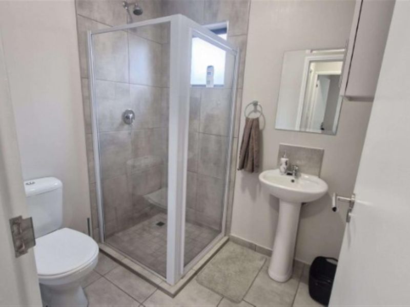 A functional bathroom featuring a pedestal basin, a corner shower enclosure with tiled walls, and a standard toilet.