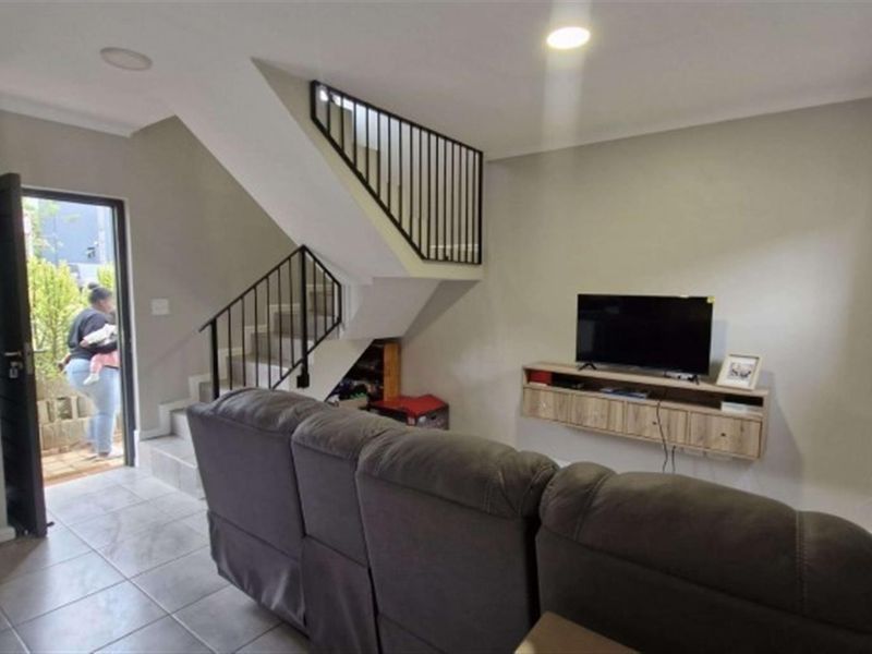 Open plan living area featuring a staircase with metal balustrade, tiled flooring, and a wall-mounted media console.