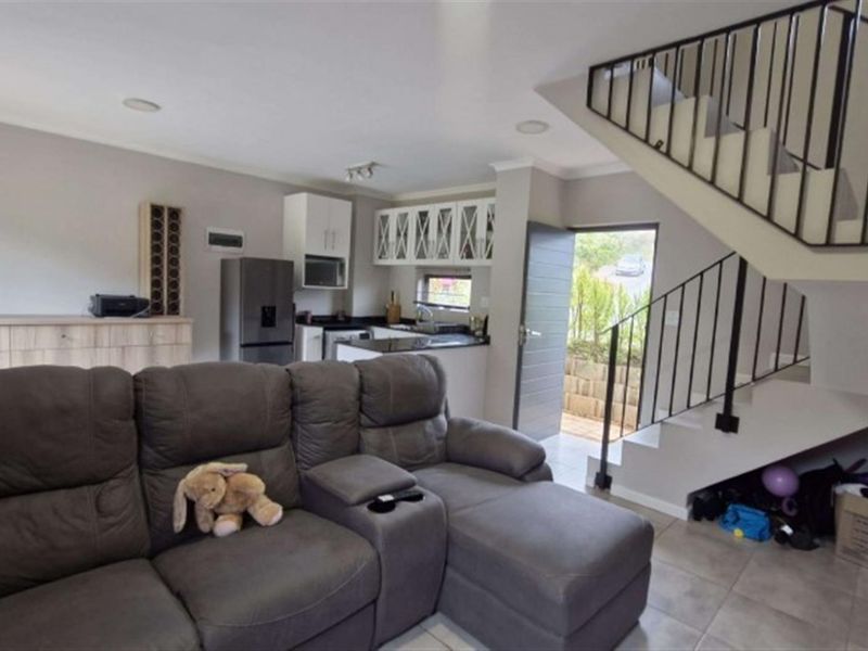 Open-plan living area featuring a compact kitchen with built-in cabinetry, tiled flooring, and a staircase leading to the upper level.