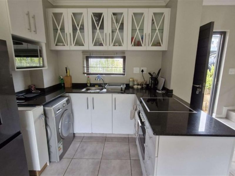 Modern kitchen featuring white cabinetry, contrasting black granite countertops, integrated appliances, and tiled flooring, offering a clean and functional workspace.