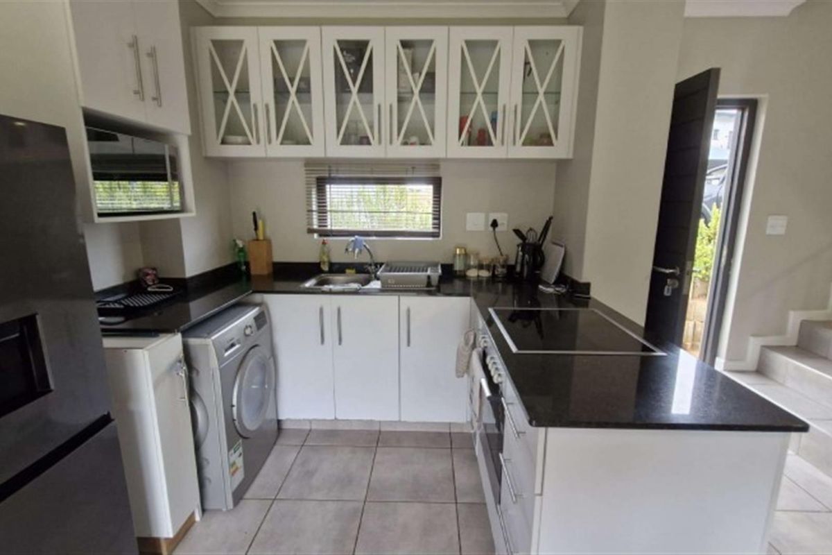Modern kitchen featuring white cabinetry, contrasting black granite countertops, integrated appliances, and tiled flooring, offering a clean and functional workspace.
