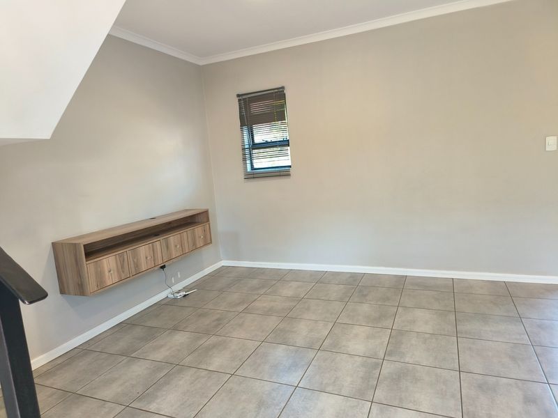 A bright, empty living room featuring neutral wall tones, modern tiled flooring, and a sleek wall-mounted storage unit.