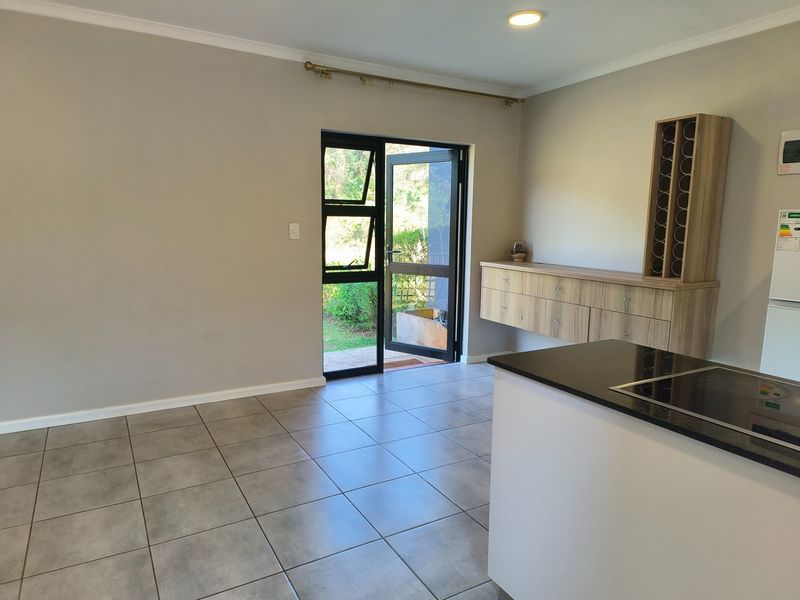 Open plan living area featuring tiled floors, built-in cabinetry with a wine rack, and direct access to the garden through a glass door.