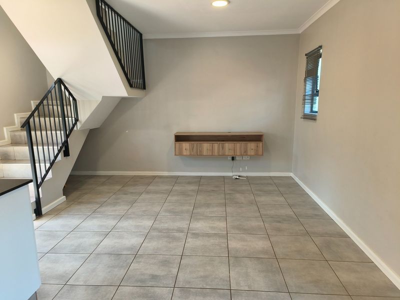 An open-plan living area featuring neutral tiled flooring, a modern wall-mounted media console, and a staircase with a sleek metal balustrade.