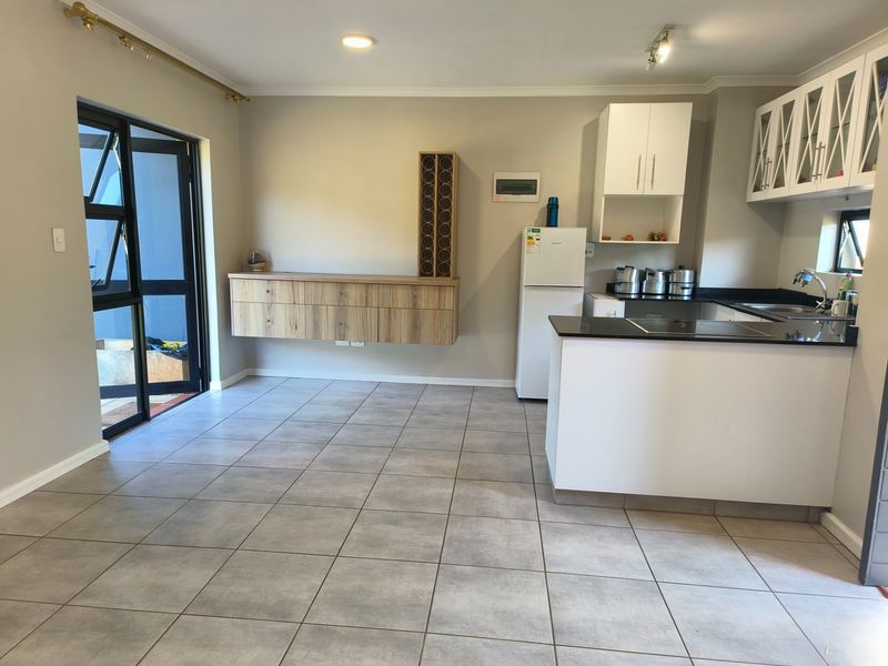 Modern open-plan kitchen and living area featuring tiled floors, sleek cabinetry, black granite countertops, and direct access to an outdoor space.