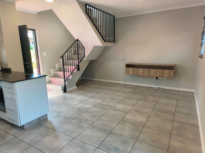 Open-plan living area featuring tiled floors, a modern staircase with metal balustrades, and a kitchen island, offering a clean and versatile space.