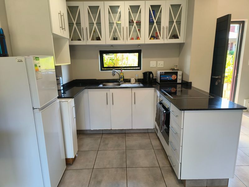 Compact kitchen featuring white cabinetry, granite countertops, built-in oven and hob, and tiled flooring with direct access to an exterior door.