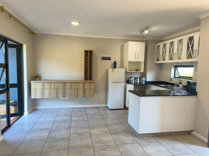 Open-plan kitchen and living area featuring modern white cabinetry, granite countertops, tiled flooring, and direct access to the outdoor space via sliding glass doors.