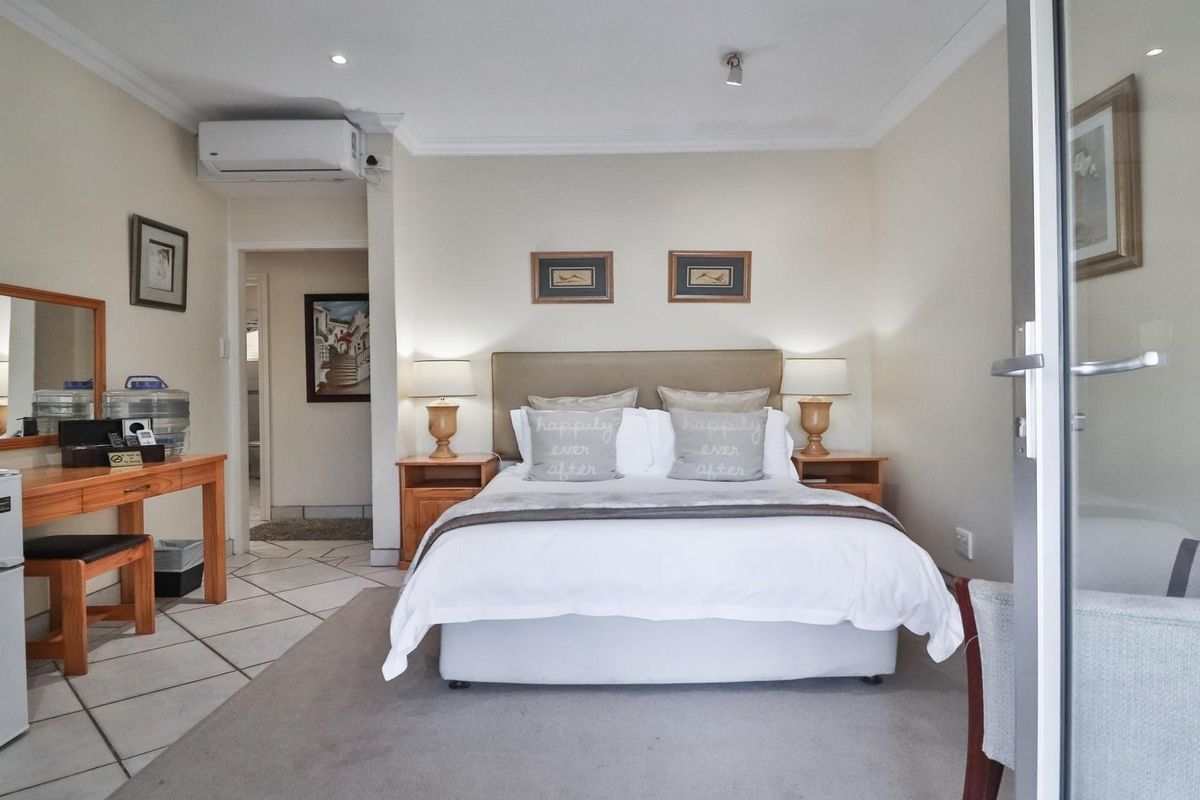 A well-maintained bedroom featuring tiled flooring, a wall-mounted air conditioning unit, and an en-suite bathroom access.