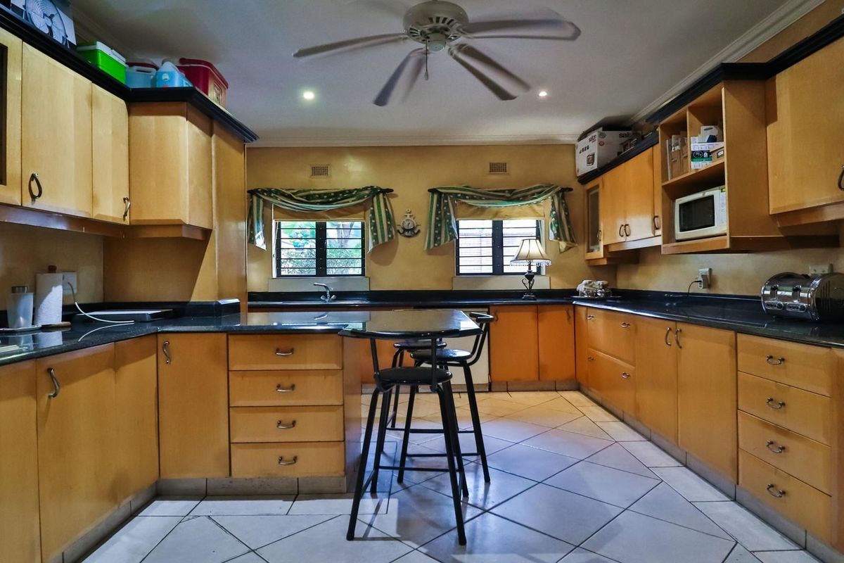A functional kitchen featuring light wood cabinetry, dark granite countertops, a central breakfast bar, and integrated ceiling fan.
