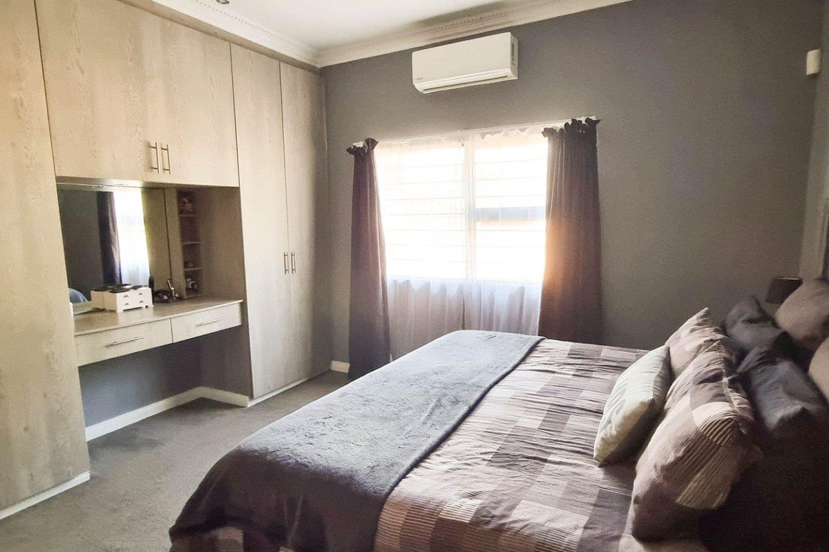 A well-maintained bedroom featuring extensive built-in cabinetry with an integrated vanity unit, neutral carpeting, and a wall-mounted air conditioning unit.