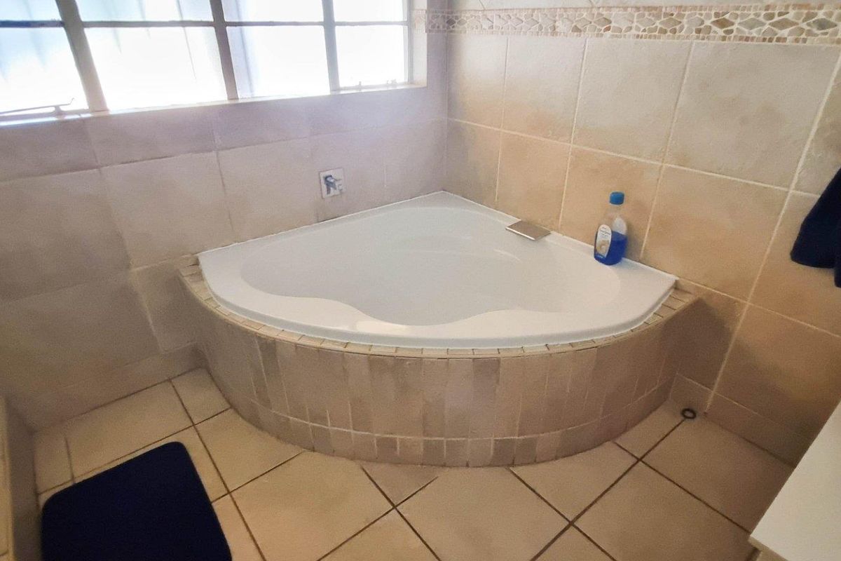 A bathroom featuring a corner bathtub with tiled surround, ceramic floor tiles, and a vessel sink vanity.