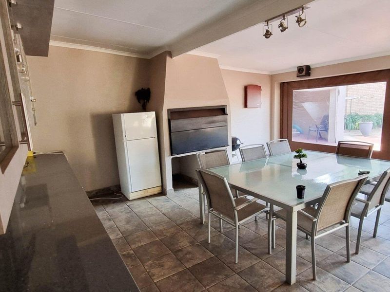 Spacious open-plan entertainment area featuring a built-in indoor braai, tiled flooring, and direct access to the outdoor patio through large glass doors.