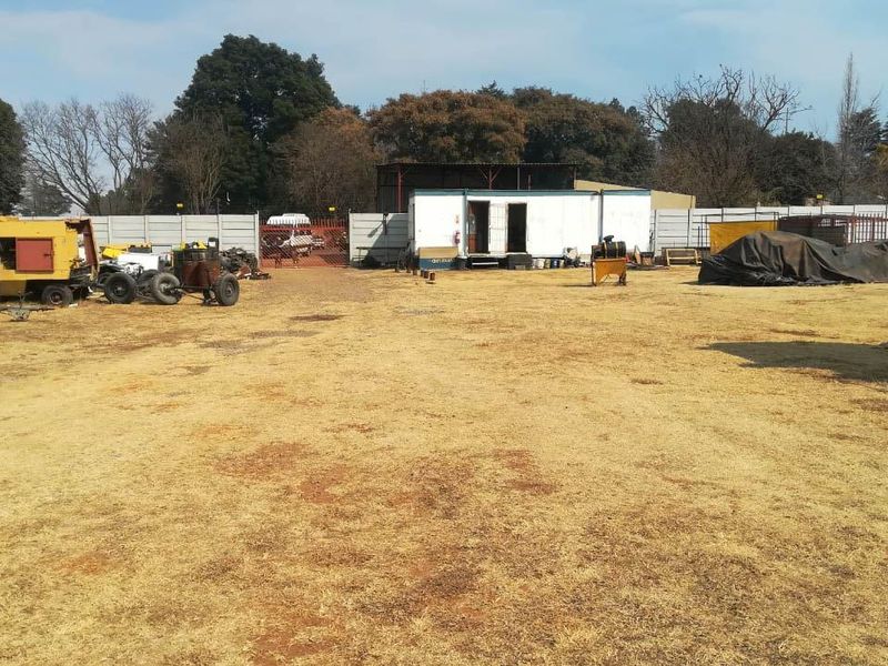 An expansive industrial yard featuring a perimeter wall, gated access, and a modular office or utility unit situated on a large open plot.