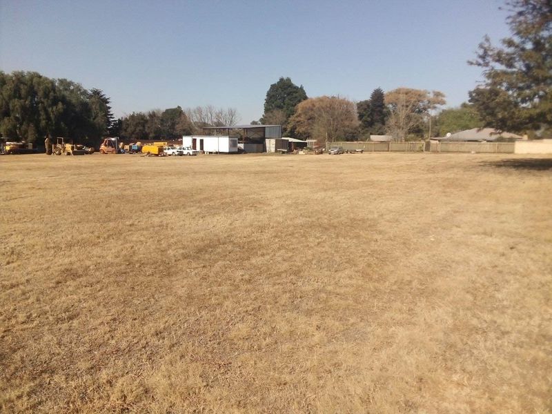 Expansive industrial land plot featuring open space, perimeter fencing, and existing auxiliary structures in the distance.