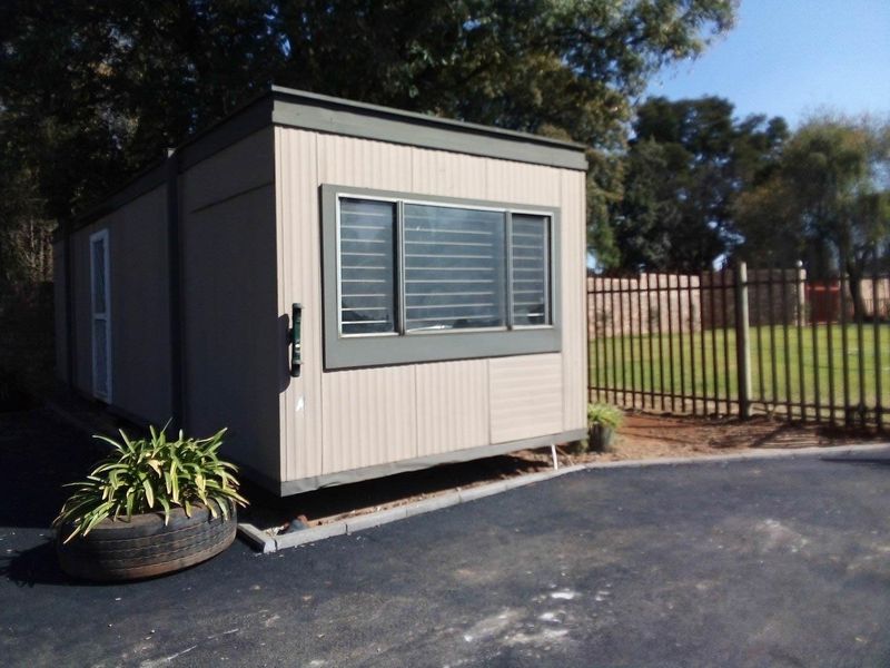 A portable industrial-style unit featuring corrugated metal cladding and horizontal sliding windows, situated on a paved area with perimeter fencing.