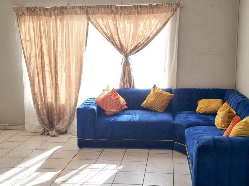A living room featuring tiled flooring and a large window with curtain fixtures, providing natural light to the space.
