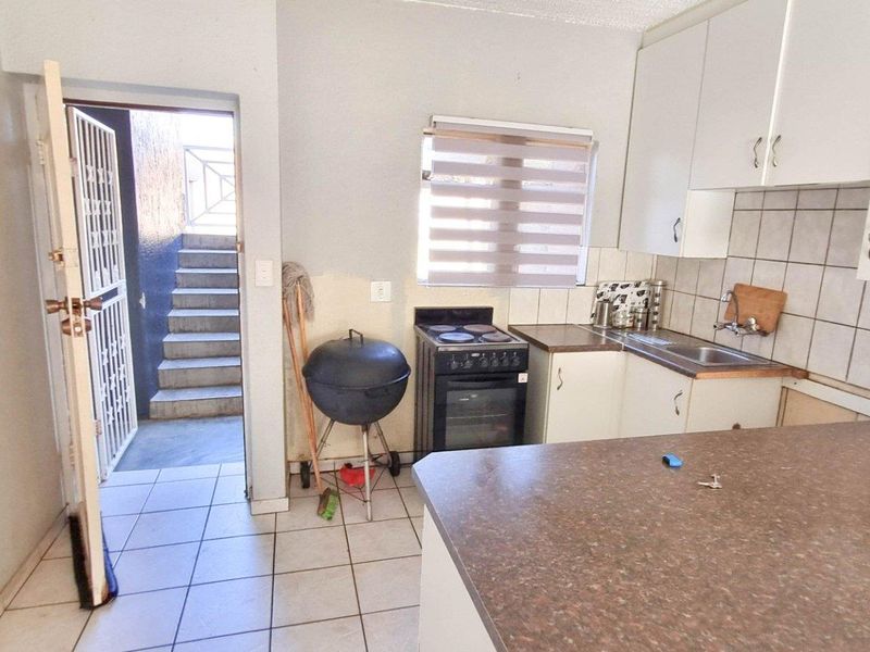 Compact kitchen featuring white cabinetry, tiled backsplash, built-in stove, and direct access to an external staircase.