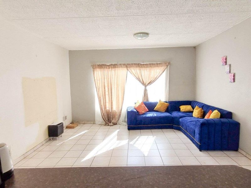 An open-plan living area featuring tiled flooring and a large window with natural light, providing a versatile space for relaxation and dining.
