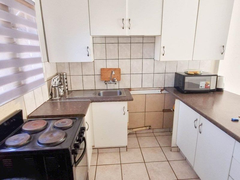 Compact kitchen featuring white cabinetry, tiled backsplash, laminate countertops, and a freestanding electric stove, requiring some maintenance and finishing touches.