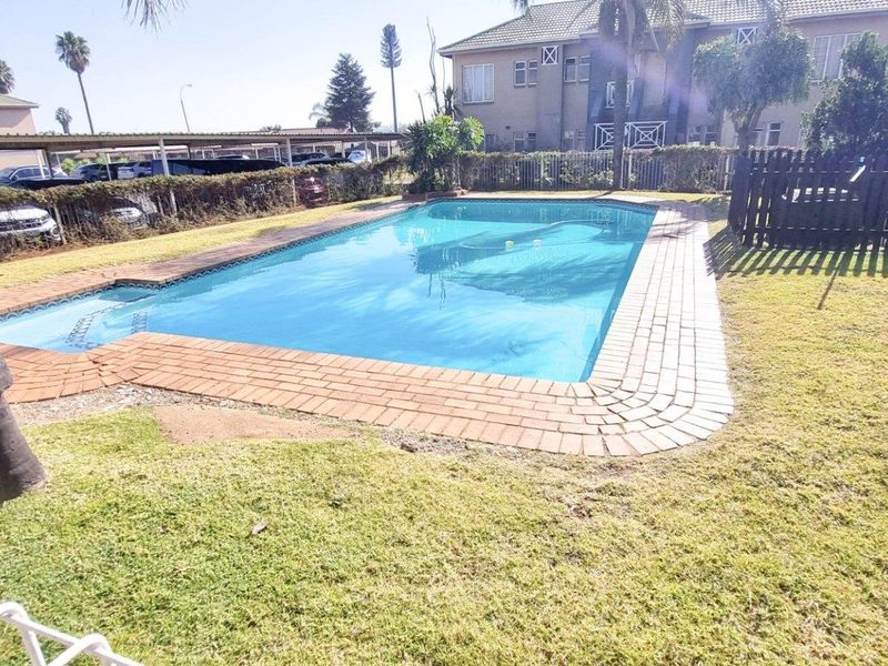 Communal swimming pool area featuring a paved brick surround and surrounding lawn within an apartment complex setting.