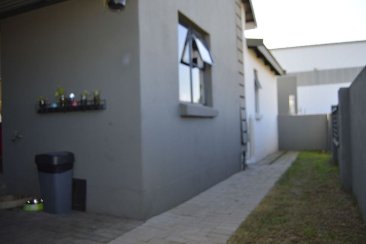 Side exterior view of the house featuring paved walkway, grey rendered walls, and window with top-hung opening mechanism.