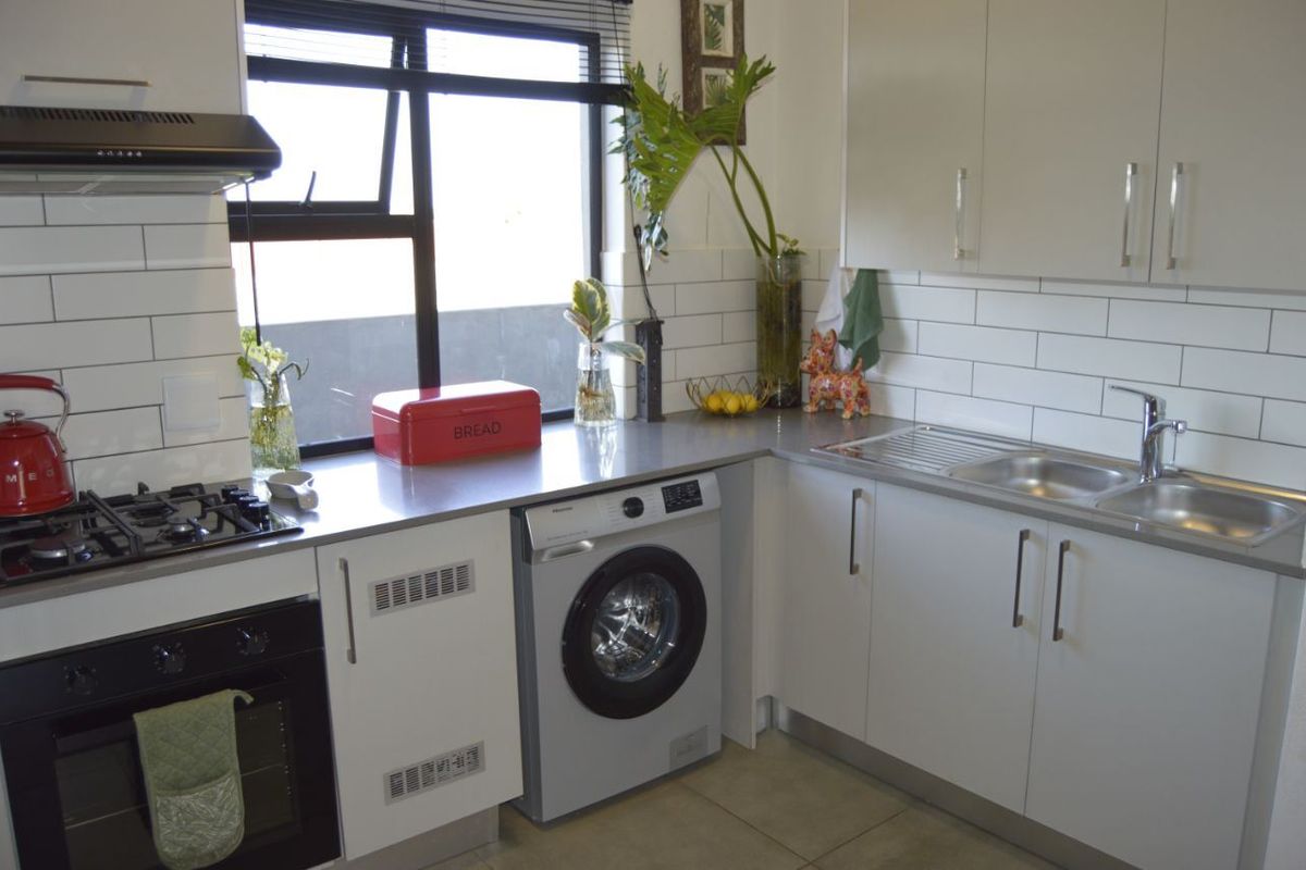Modern kitchen featuring white cabinetry, subway tile backsplash, integrated gas hob, oven, and built-in washing machine with stainless steel countertops.