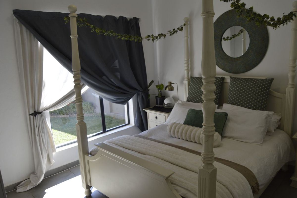A well-maintained bedroom featuring a four-poster bed frame, tiled flooring, and a large window providing natural light and garden views.