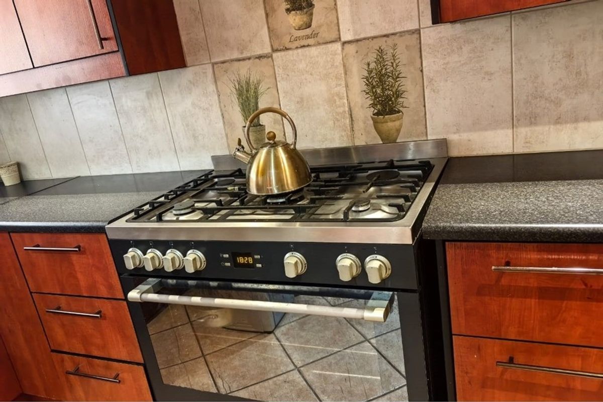 A functional kitchen area featuring a built-in gas stove and oven, dark granite countertops, and wood-finish cabinetry with a tiled backsplash.