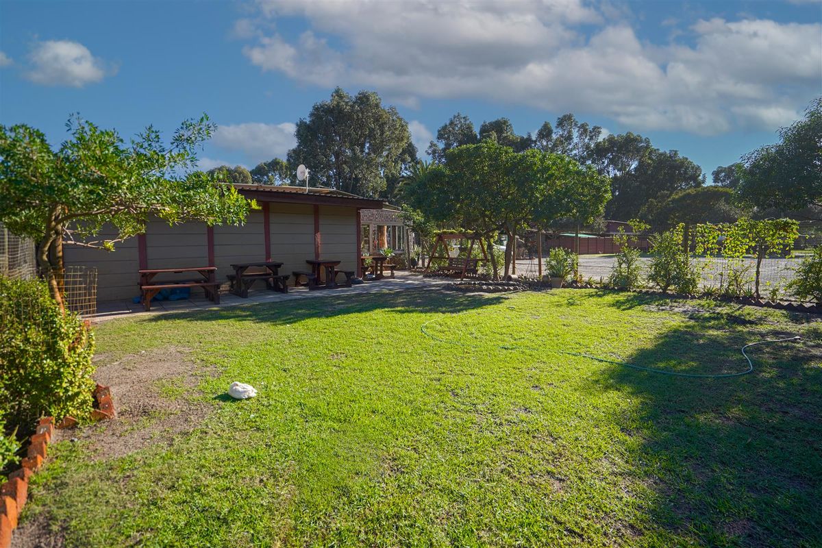 A spacious rear garden area featuring a lawn, mature trees, and a covered patio space attached to the lodge building.