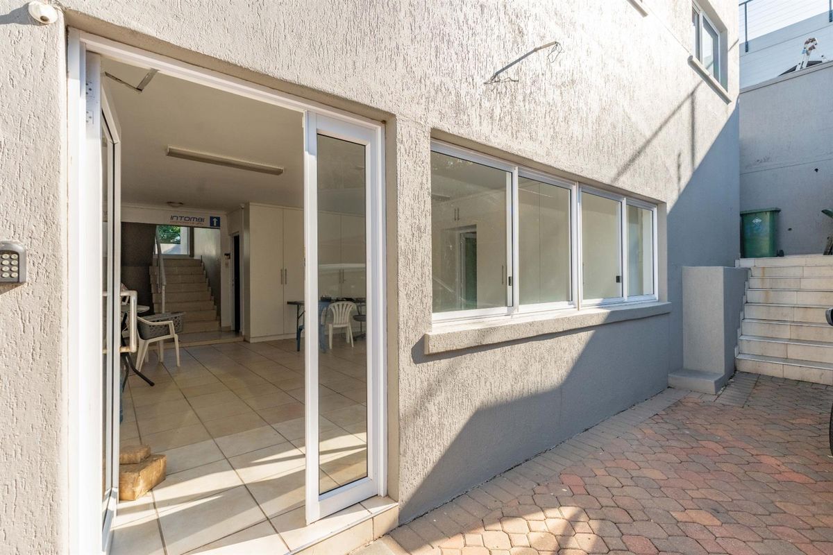 View of the exterior rear facade featuring a paved courtyard, sliding glass doors, and access to an interior open-plan space with tiled flooring.