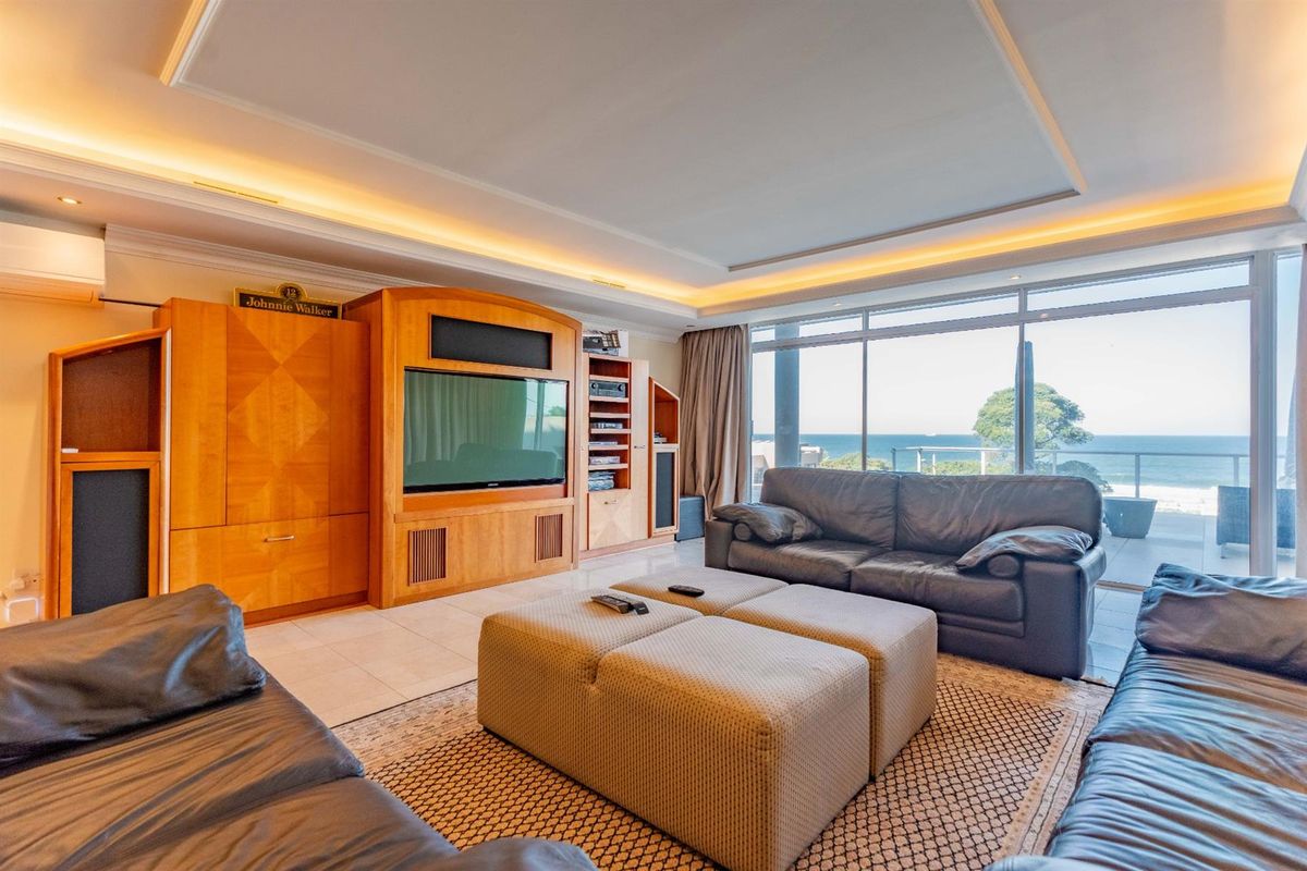 Spacious living room featuring recessed tray ceiling with ambient lighting, large floor-to-ceiling windows, and direct access to a balcony with ocean views.