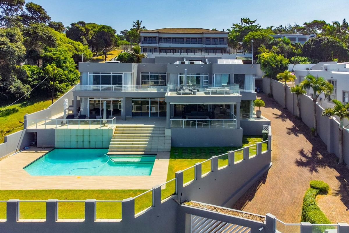 Aerial view of a modern multi-level residence featuring a swimming pool, expansive terraces, glass balustrades, and landscaped garden areas.