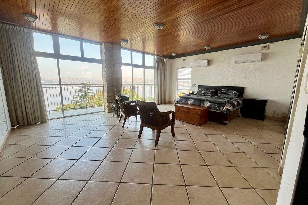 Spacious bedroom featuring a wood-paneled ceiling, tiled flooring, dual air conditioning units, and large sliding glass doors opening to a balcony with scenic views.