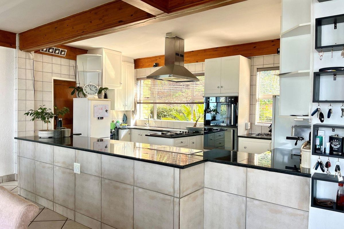 A functional kitchen featuring a large breakfast bar with granite countertops, built-in oven, stainless steel extractor fan, and exposed timber ceiling beams.