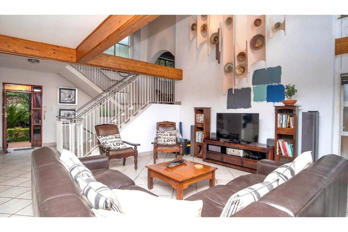 Spacious living room featuring exposed timber ceiling beams, a staircase with metal balustrade, and tiled flooring, offering an open-plan layout with garden access.