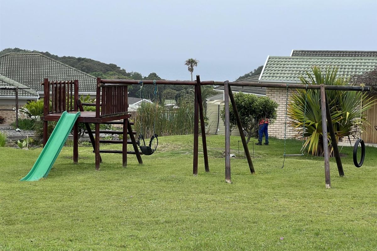 A residential garden featuring a wooden jungle gym with a slide and swing set, set against a backdrop of neighboring properties.