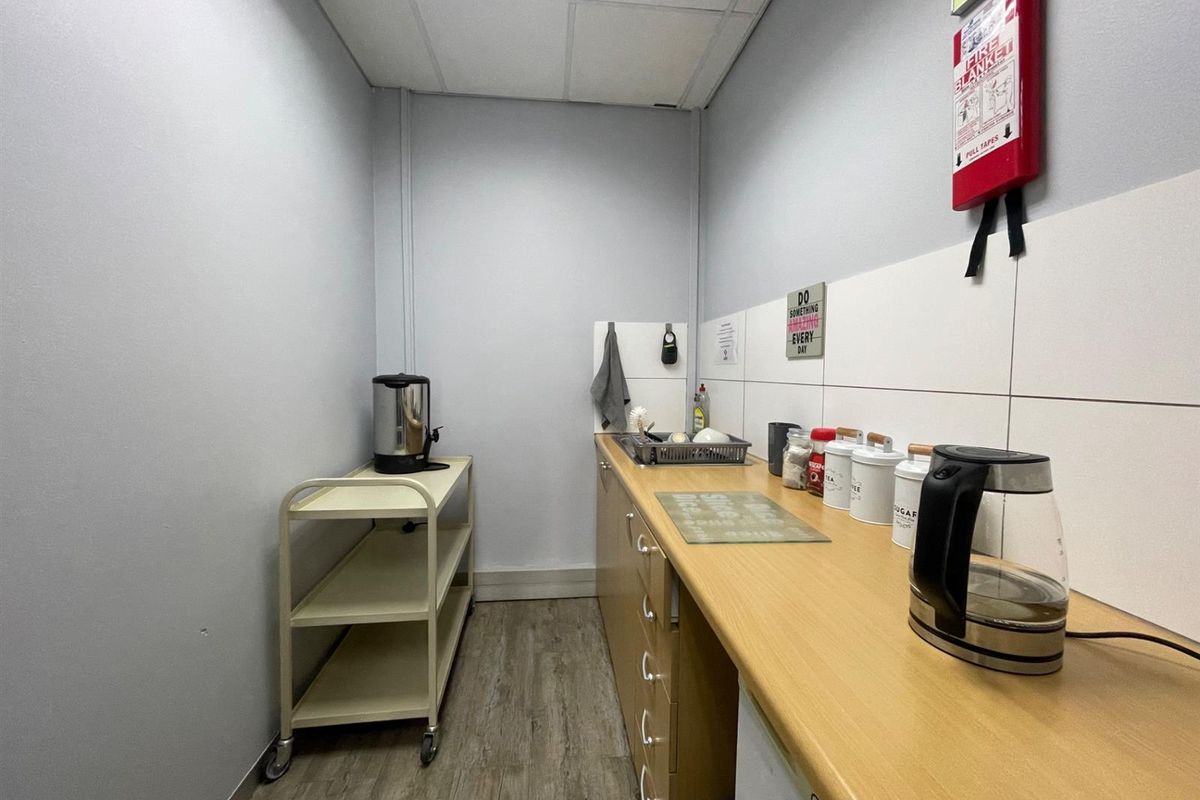 A functional office kitchenette featuring laminate countertops, built-in cabinetry, and a tiled splashback, providing a practical space for staff refreshments.