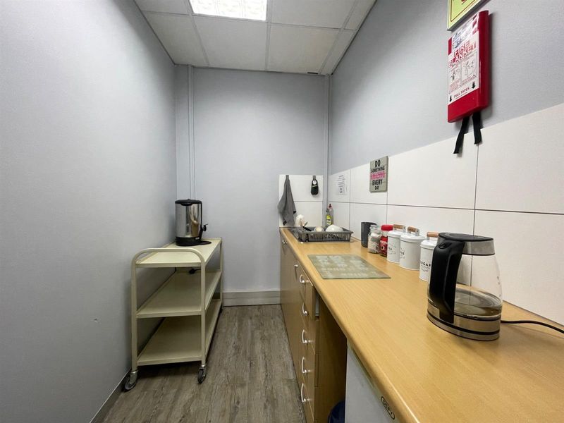 A functional office kitchenette featuring laminate countertops, built-in cabinetry, and a tiled splashback, providing a practical space for staff refreshments.