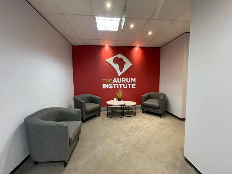A professional office reception or waiting area featuring a branded accent wall, recessed ceiling lighting, and neutral carpeting.