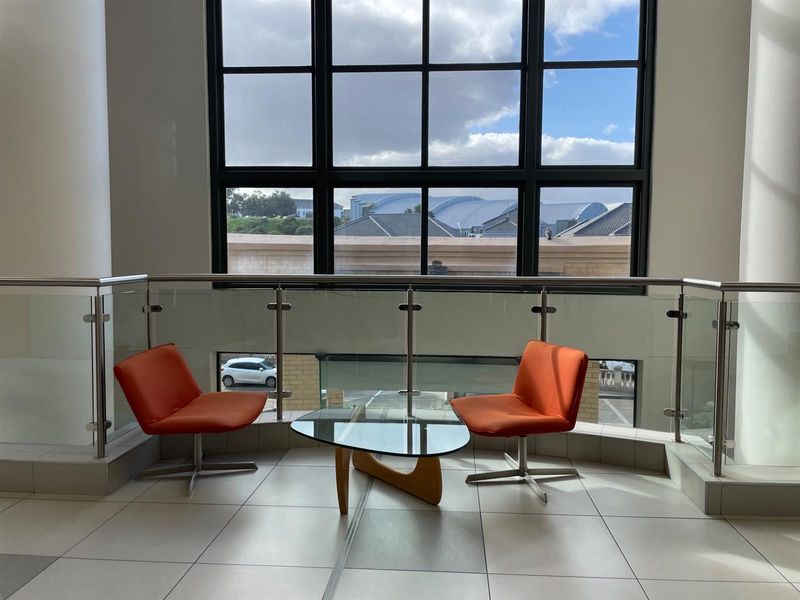 A bright office landing area featuring large grid windows, modern glass and stainless steel balustrades, and clean tiled flooring.