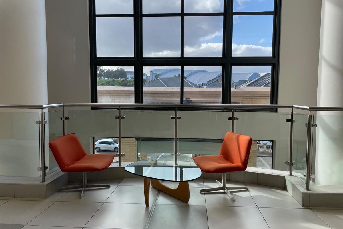A bright office landing area featuring large grid windows, modern glass and stainless steel balustrades, and clean tiled flooring.