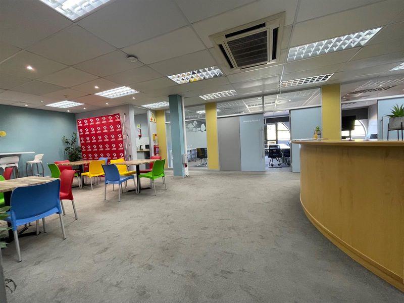 Open-plan office space featuring a reception desk, glass-partitioned meeting rooms, suspended ceilings with integrated lighting, and ducted air conditioning.