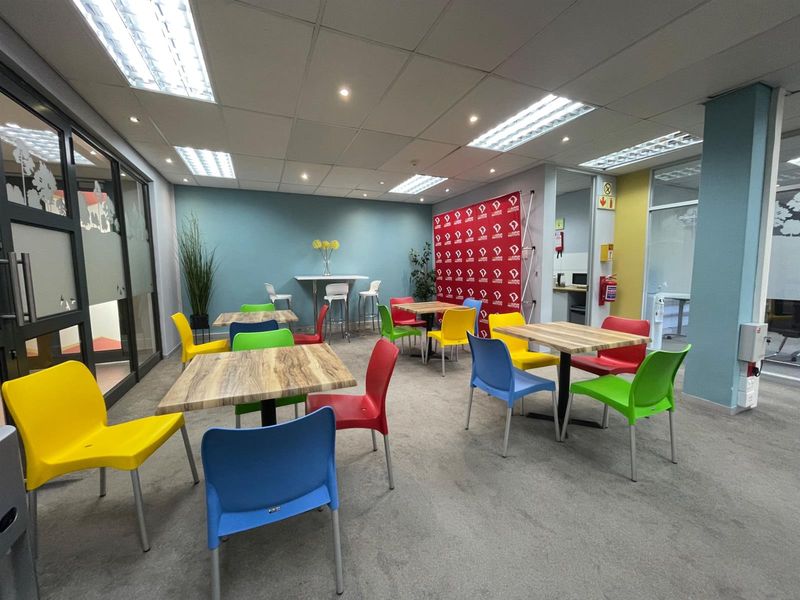 A functional office break-out or communal area featuring suspended ceilings, recessed lighting, and glass partitioning, suitable for collaborative work or meetings.