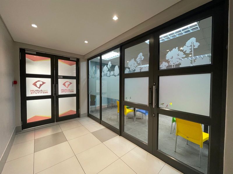 Modern office interior featuring glass partition walls with frosted decals, recessed downlighting, and clean tiled flooring in a professional corporate environment.