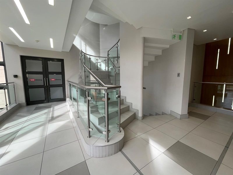 Modern office building entrance lobby featuring a prominent curved staircase with glass balustrades and clean, neutral tiled flooring.